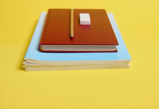 A rubber, pencil on a book with hardcover , textbooks, isolated on yellow background with copy space