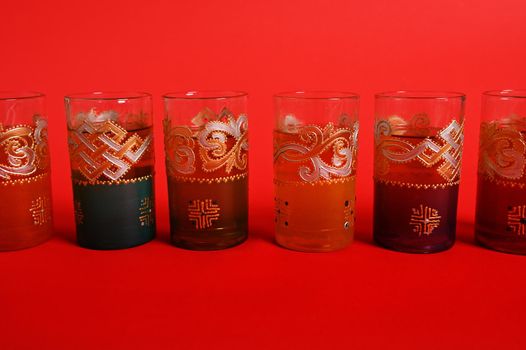 Multicolored glasses for Moroccan green mint tea, decorated in oriental style. Isolated on red background