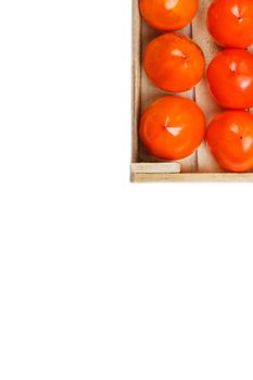 Juicy ripe persimmon in a large wooden box on a white background.