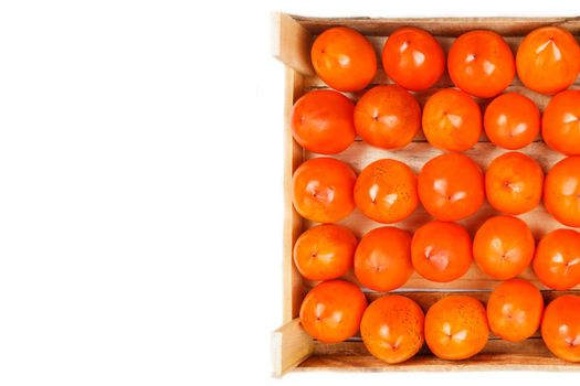 Juicy ripe persimmon in a large wooden box on a white background.