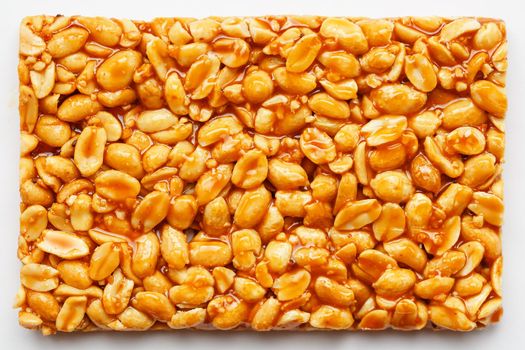 A large tile of roasted peanuts bar in a sweet molasses on a white background. Kozinaki useful and tasty sweets of the East