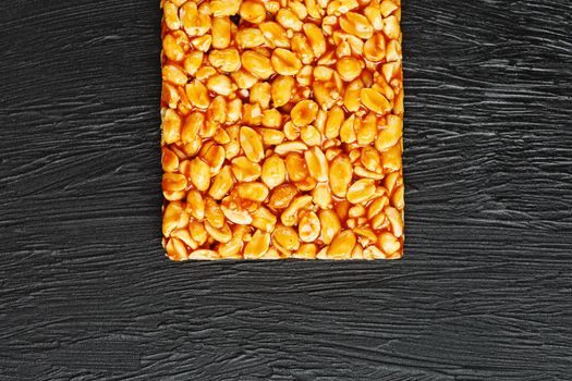 A large golden tile of peanuts, a bar in a sweet molasses on a black texture background. Kozinaki useful and tasty sweets of the East