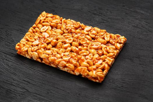 A large golden tile of peanuts, a bar in a sweet molasses on a black texture background. Kozinaki useful and tasty sweets of the East