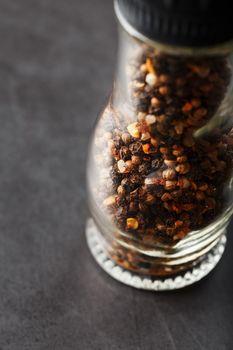A mixture of peppercorns seasoning and salt in a transparent mill close-up