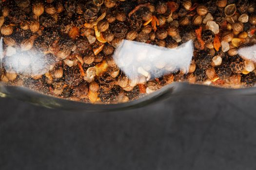 A mixture of seasonings, spices and herbs in a glass mill on a black background.