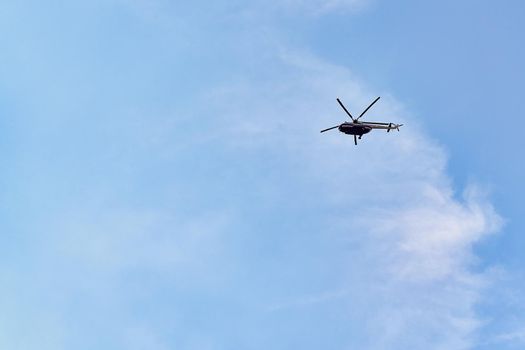 Flying helicopter against the background of a blue sky with spruce clouds