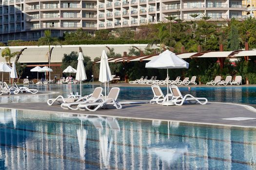 Pool with blue water, sun loungers and parasols in the background of the hotel