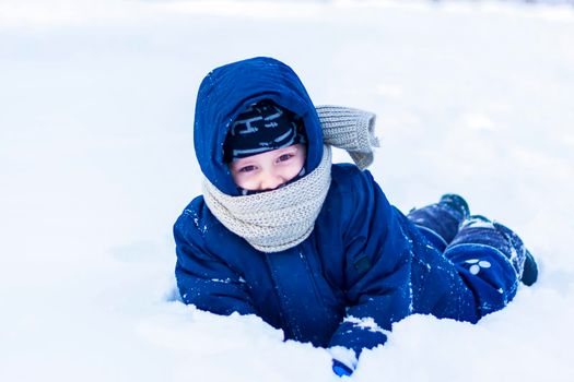 A smiling happy child lies in a snowdrift on a sunny winter day. A lot of snow and very frosty. Active winter outdoor games. 