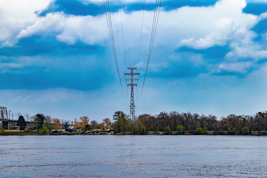 Wires of a high-voltage power line tower over a river.