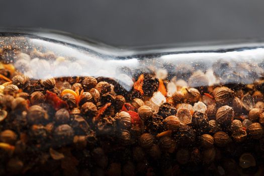 A mixture of peppercorns seasoning and salt in a transparent mill close-up
