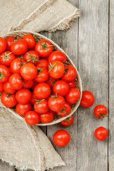 Small red tomatoes in a wicker basket on an old wooden table. Ripe and juicy cherry
