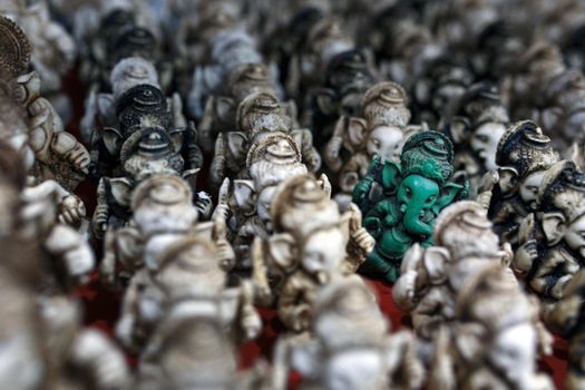 The stone statuette of Ganesh is green, contrasting with the group of light Ganesh on the counter of the Indian market
