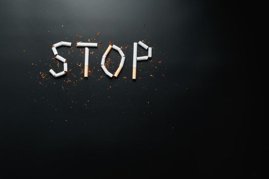 The inscription STOP from cigarettes on a black background. Stop smoking. The concept of smoking kills. Motivation inscription to quit smoking, unhealthy habit.