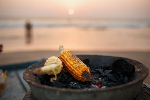 Golden Corn cobs on the coals in the grill. On the Arambol beach at sunset. Asian, Indian street food