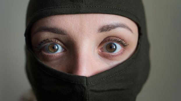 Female portrait of young girl wearing khaki balaclava, only eyes are visible, mandatory conscription, military, feminism, equality concept