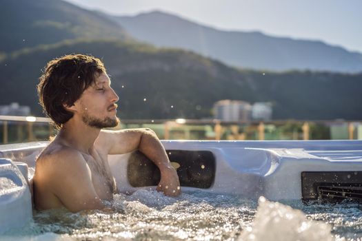 Portrait of young carefree happy smiling man relaxing at hot tub during enjoying happy traveling moment vacation life against the background of green big mountains
