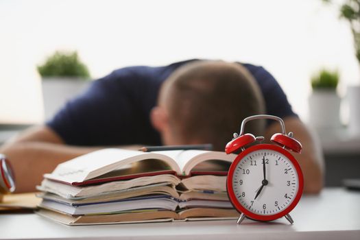 Tired student take nap behind pile of textbooks on table