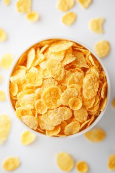 White cup with golden corn flakes, isolated on white background. Hopya crumbled around the cup. View from above