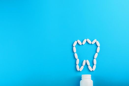 White Vitamins with calcium Ca, D3 in the form of a tooth scattered from a white jar on a blue background