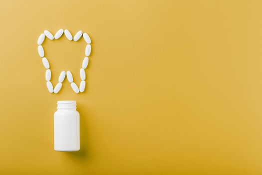 Calcium vitamin in the form of a tooth spilled out of a white jar on a yellow background.