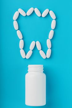 Vitamins with calcium Ca in the form of a tooth are scattered from a white jar on a blue background