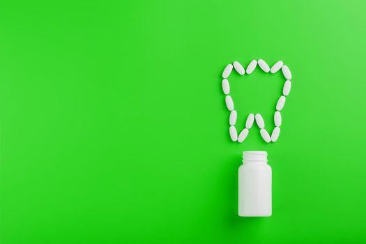 Calcium vitamin in the form of a tooth spilled out of a white jar on a Green background.