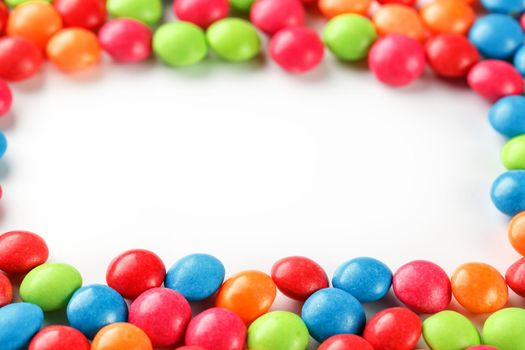 Frame of multi-colored candies close up. Rainbow colored dragee multicolored glaze on a white background
