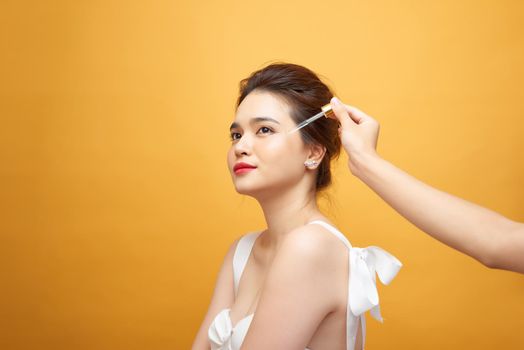portrait of young woman applying serum on her face on yellow background