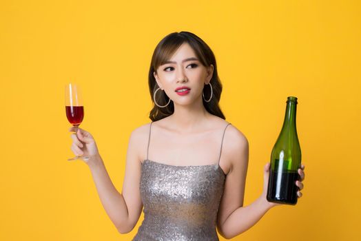 Woman in shining dress with alcohol on yellow background.