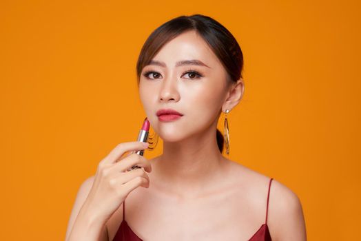 Attractive girl rouging her lips with red lipstick. Isolated on yellow background