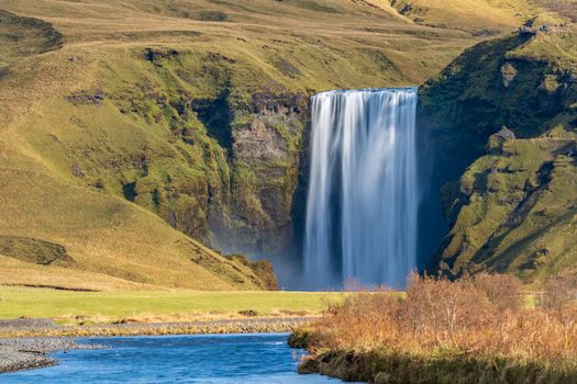 Long exposure of famous Skogafoss waterfall from the distance with hikers on top viewpoint