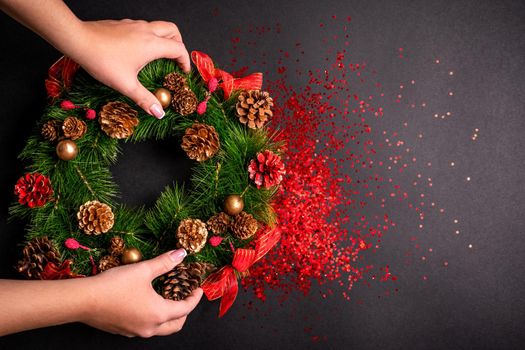 Female hands holding christmas wreath over black background with glitter and copy space