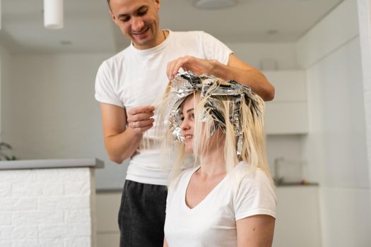 Professional male hairdresser dyes hair woman