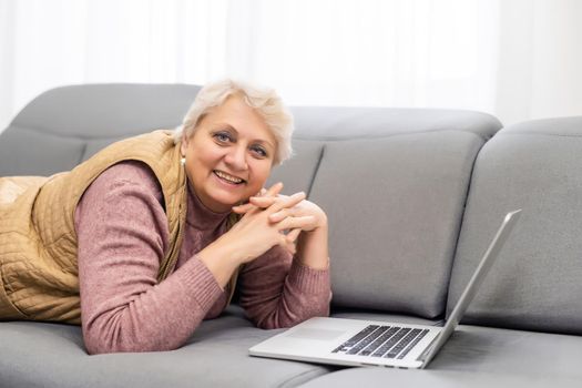 Serious mature older adult woman watching training webinar on laptop working from home or in office. 60s middle aged businesswoman taking notes while using computer technology