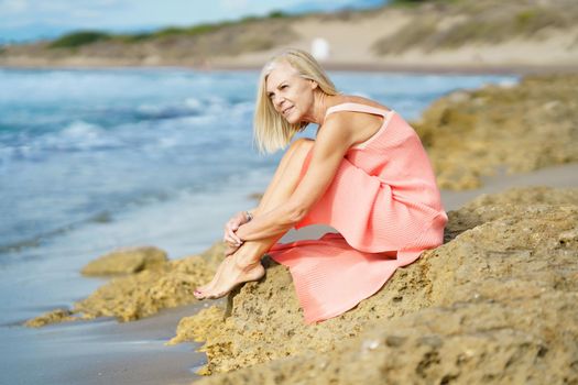 Slim senior woman on rocky seashore in summer