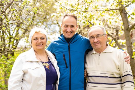 Adult son with his elderly parents outdoors in a natural setting.
