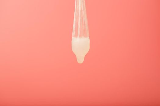 Condom that missed a drop of sperm, used contraceptive on a red background. Soft contrast