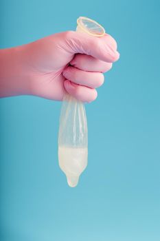 Latex condom contraception with sperm, a doctor in a pink glove holds a full used condom on a blue background