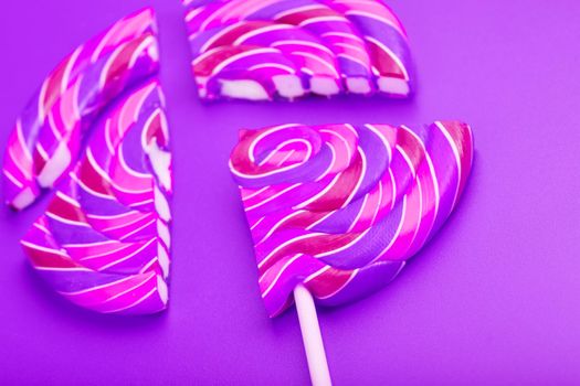 Pink Lollipop split into pieces on a pink background, top view, close-up.