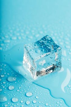 Ice cube with water drops on a blue background. The ice is melting.