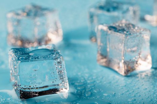 Ice cubes are scattered with water drops scattered on a blue background. Close up.