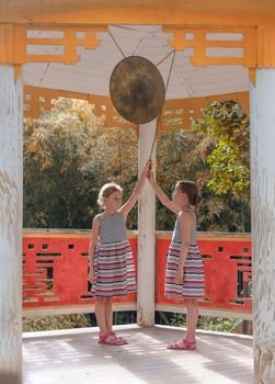 Two tween caucasian girls beating gong in classical chinese pavilion