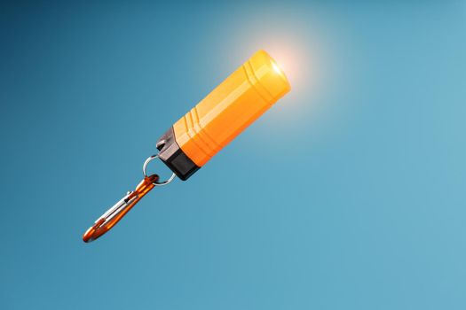 Orange led Flashlight with a carabiner on a blue background. LED lights in flight.