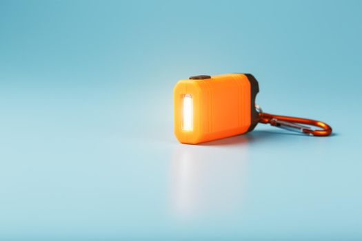An orange led flashlight with a carabiner glows on a blue background.