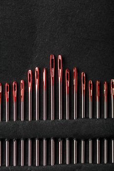 Sewing needles of different sizes in a set of red on a black background.