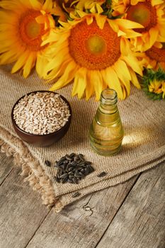 Sunflower oil in a bottle with sunflower seeds and flowers on a wooden background.
