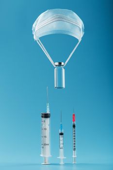 An ampoule with a vaccine against the virus on a shroud of protective grease on a blue background goes down to a row of syringes.