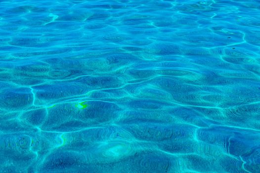 Marine background. Transparent turquoise-blue sea water against the background of white sand below, top view. Sun glare on the surface. High quality photo