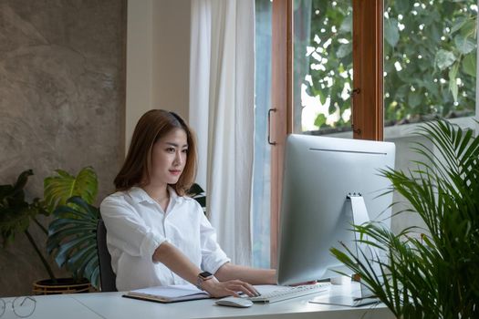 Thinking about business. Thoughtful young woman looking at computer screen while sitting at his working place at home. Working remotely
