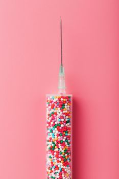 Medical Syringe filled with colorful balloons on a pink background with free space.